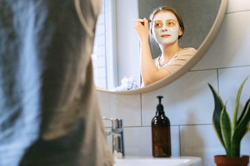 A woman applies a clay mask using a brush, promoting skincare and self-care routines.