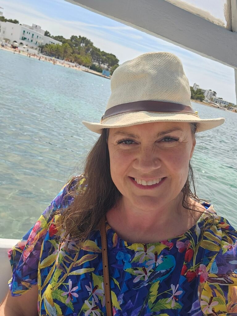 Rosaleen wearing a summery dress and sunhat posing next to the sea